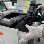 Worker replacing printer ink cartridge in a laboratory environment, highlighting technology maintenance.